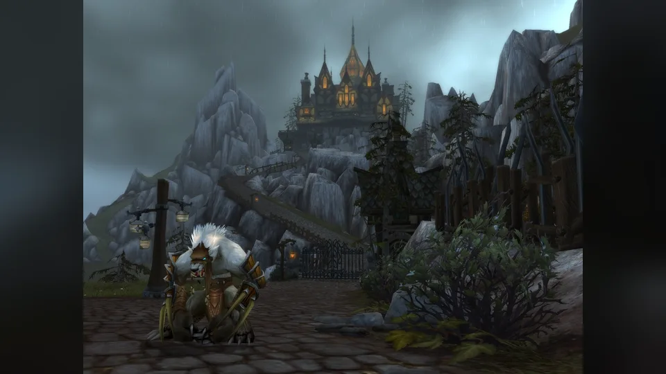 A worgen stands in a rainy cobbled street in Gilneas with a lit mansion on the hill behind.